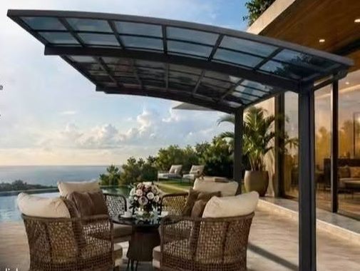 Render of a dark aluminium carport with a curved glazed roof over a terrace with wicker chairs and a view of the sea