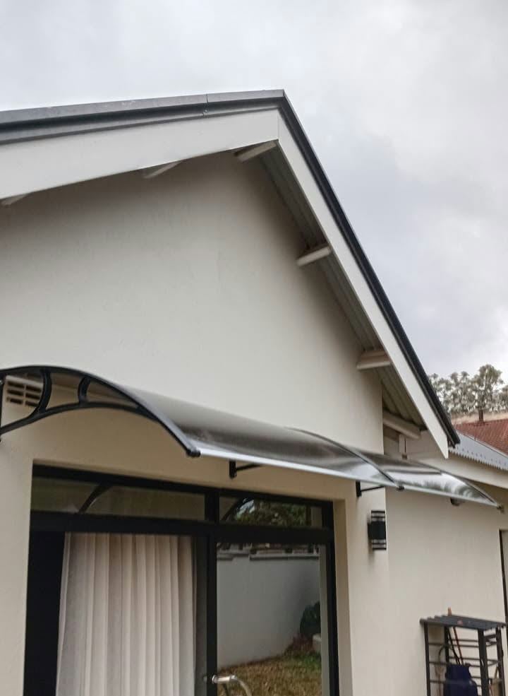A smoked polycarbonate awning curving over a glass door on a cream house with a gabled roof