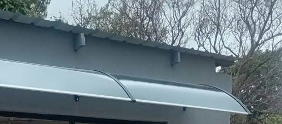 A two-panel grey polycarbonate awning across the front of a small grey building